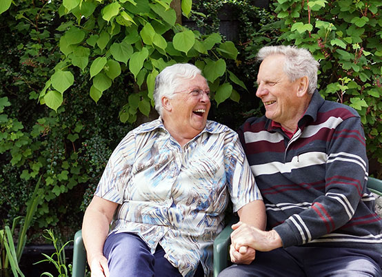 Een ouder echtpaar lachend in hun tuin